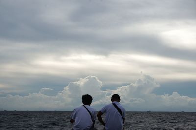 Rear view of male friends sitting bay against cloudy sky