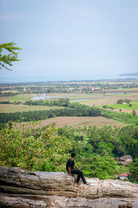 Rear view of man sitting on rock against sky