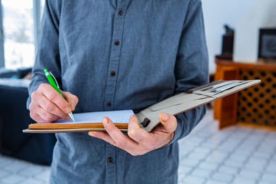 Midsection of man holding paper while standing against wall