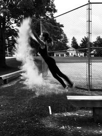 Side view of teenage girl throwing chalk powder while jumping on bench in park