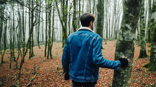 Boy with blue jeans jacket walks in autumn forest with fog