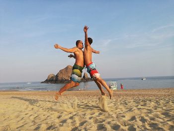 Boy jumping on beach against sky