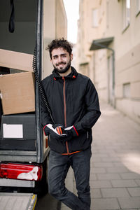 Portrait of confident young delivery man with boxes in truck