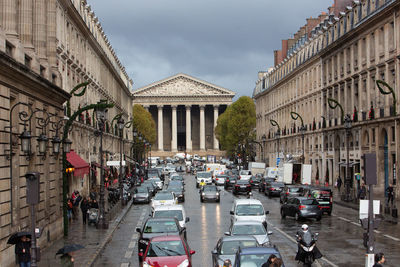 Cars on city street by buildings against sky