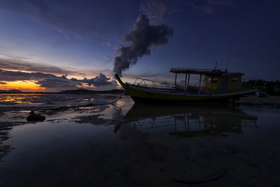 Boat moored on beach against sky during sunset