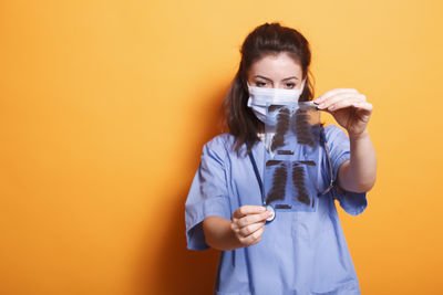 Portrait of female doctor standing against yellow background