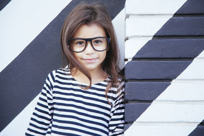 Portrait of smiling girl wearing eyeglasses against wall