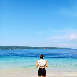 Rear view of woman standing at beach against sky