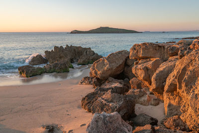 Rocks on beach against sky during sunset