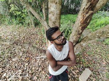 Young man standing by tree trunks in forest