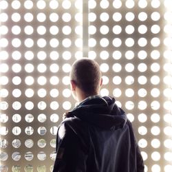 Rear view of man looking through metal grate