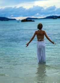 Rear view of woman standing in sea against sky