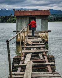 Rear view of man standing by lake against sky