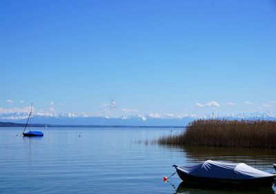 Boats moored in lake against blue sky