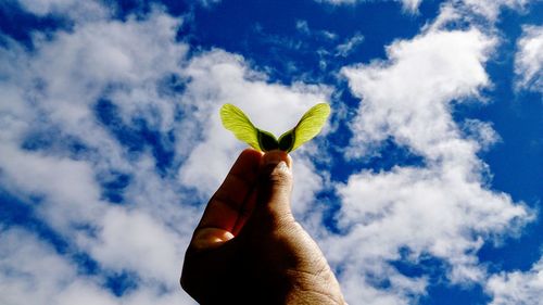 Low angle view of human hand against cloudy sky