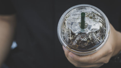 Close-up of hand holding plastic glass with  cold drink and straw
