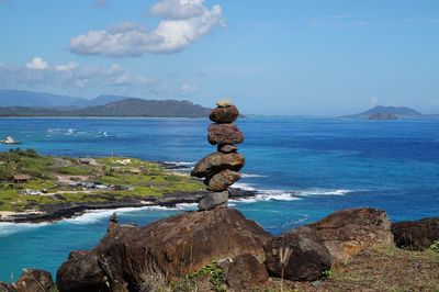 Stack of rocks on shore by sea against sky