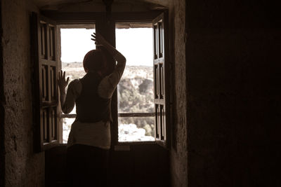 Rear view of man looking through window at home