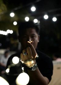 Close-up of man holding wineglass against illuminated lights