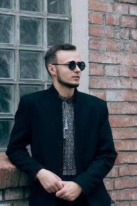 Young man wearing sunglasses while standing against brick wall