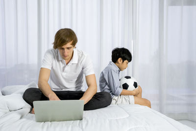 Young woman using mobile phone while sitting on bed