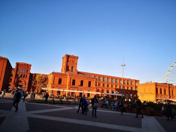 Group of people walking in front of building against sky