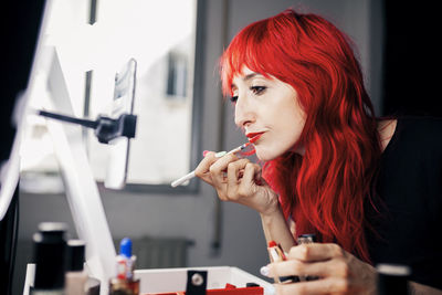 Beautiful female make-up artist applying lipstick while vlogging at studio