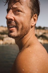 Side view of shirtless man looking away while enjoying vacation at beach on sunny day