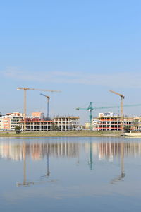 Reflection of construction site on water against clear sky