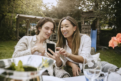 Smiling young woman using phone while sitting on table
