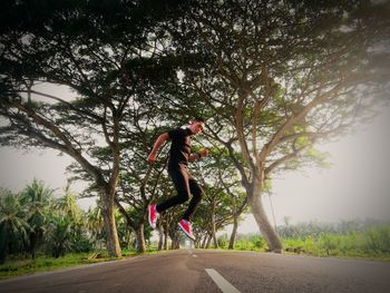 Man levitating over road amidst trees during sunset