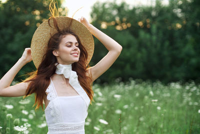 Young woman wearing hat standing against plants