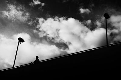 Low angle view of silhouette person standing on bridge against cloudy sky