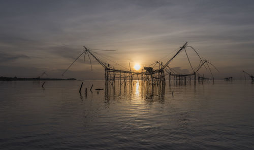 Silhouette of fishing net in sea against sunset sky