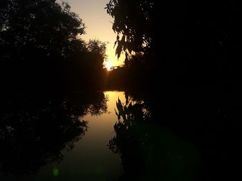 Silhouette trees by lake against sky during sunset