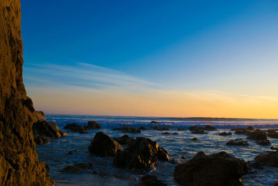 Rocky shore and sea against sky during sunset
