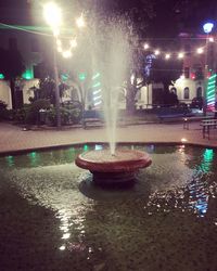 Illuminated fountain by building at night