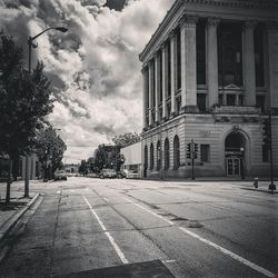 Road leading towards buildings against cloudy sky