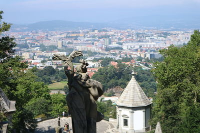 Statue amidst trees and buildings in city against sky