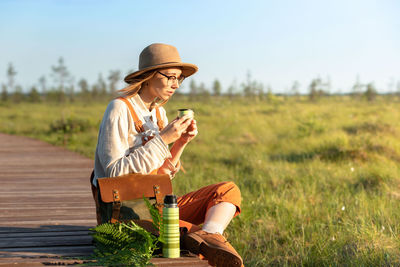 Naturalist woman resting on boardwalk, drinking tea, enjoying the moment at sunset. ecotourism