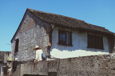 Low angle view of person standing by house against clear blue sky