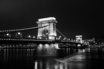 Illuminated bridge over river against sky at night