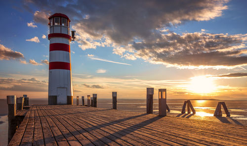 Lighthouse by sea against sky during sunset