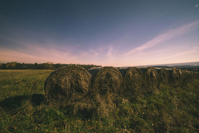 Hay bales on grassy field against sky at sunset