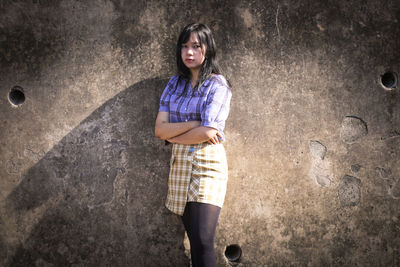 Portrait of young woman standing against wall