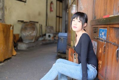 Portrait of beautiful young woman sitting outside closed house