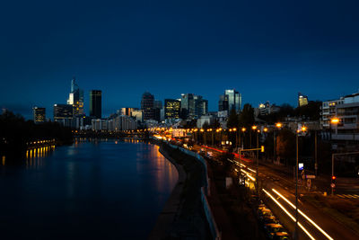 Illuminated city by buildings against clear blue sky at night