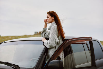 Side view of young woman sitting on car