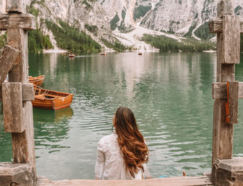 Rear view of woman sitting on pier at lake 