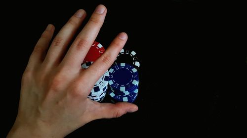 Cropped image of hand pushing gambling chips over black background